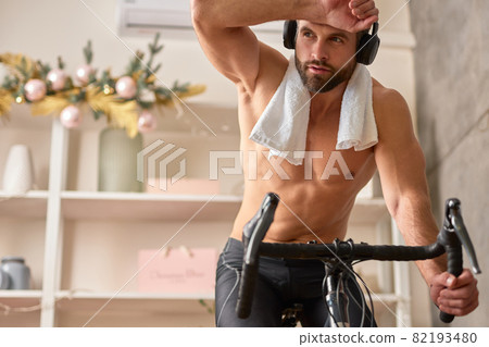 Handsome bearded man riding stationery bicycle at home Handsome bearded man riding stationery bicycle at home 82193480