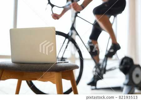 Young man riding stationary bike in room with laptop 82193513
