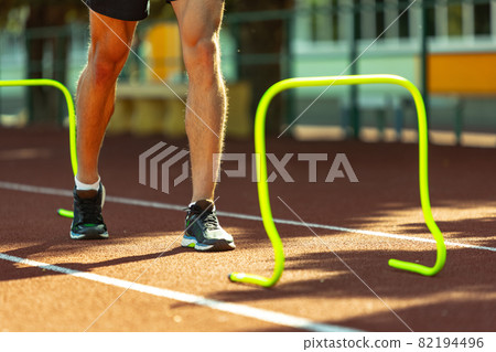 Cropped image of male athlete, runner training at public stadium, sport court or running track outdoors. Summer sport games. Man's legs 82194496