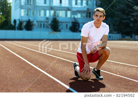One young sportive man, male athlete, runner practicing alone before race at public stadium, sport court or running track, outdoors. Professional sport games. 82194502