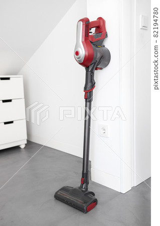 Modern Cordless vacuum cleaner leaning on a wall of a room. Homework concept Modern Cordless vacuum cleaner leaning on a wall of a room. Homework concept 82194780
