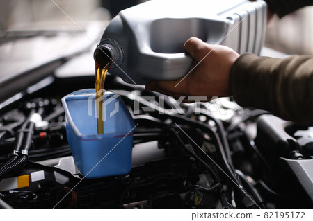 Master repairman pouring motor oil into car engine closeup 82195172