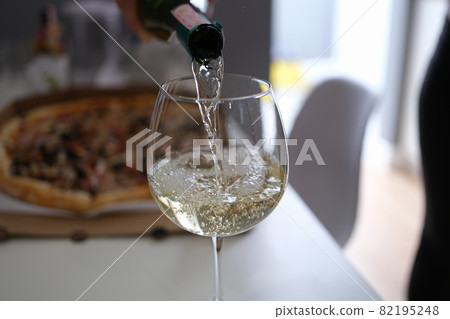 White wine pouring from bottle into glass goblet on pizza background closeup White wine pouring from bottle into glass goblet on pizza background closeup 82195248