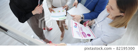 Business trainer holding documents with graphs in his hands and showing audience information on board Business trainer holding documents with graphs in his hands and showing audience information on board 82195300