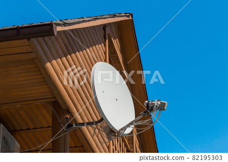 Satellite dish communication TV antenna on a wooden house against a blue sky Satellite dish communication TV antenna on a wooden house against a blue sky 82195303