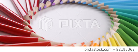 Many multi-colored wooden pencils lying in shape of circle over colors of rainbow closeup background. 82195362