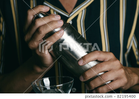 young man prepares a cocktail in a metal shaker young man prepares a cocktail in a metal shaker 82195400