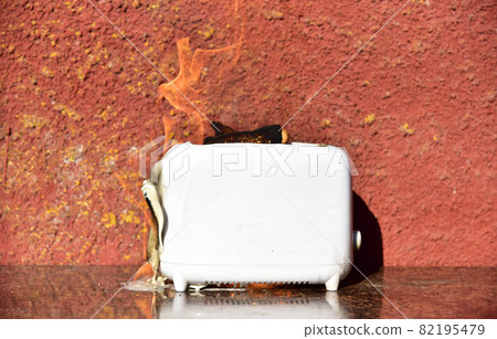 Burning toaster. Toaster with toast caught on fire over table. 82195479