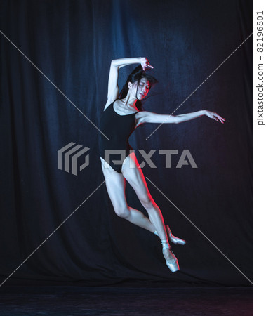 Young and graceful female ballet dancer in motion isolated on dark background in neon light. Art, motion, action, flexibility, inspiration concept. 82196801
