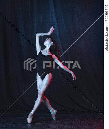 Young and graceful female ballet dancer in motion isolated on dark background in neon light. Art, motion, action, flexibility, inspiration concept. 82196841