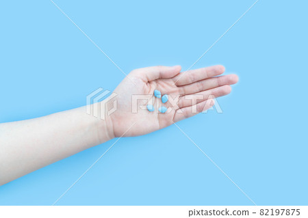 Hands holding sildenafil (Viagra) pills in blister package on blue background. Indication of sildenafil is treatment of erectile dysfunction, pulmonary arterial hypertension. 82197875