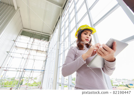 Female engineer in yellow safty helmet is looking to tablet computer 82198447