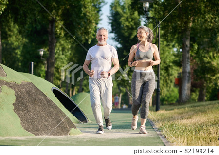 A mature couple running in the park and looking contented A mature couple running in the park and looking contented 82199214
