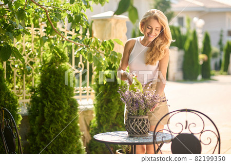 Woman watering potted flowers on table outdoors Woman watering potted flowers on table outdoors 82199350
