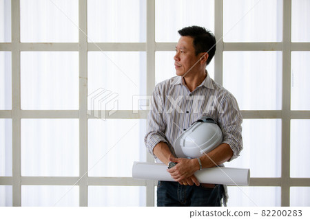 Portrait of male engineer with self-confidense and friendly manner, holding roll paper in hand Portrait of male engineer with self-confidense and friendly manner, holding roll paper in hand 82200283