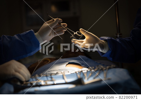 Doctors in sugery room sending medical device to other in operation 82200971