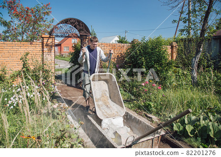 A man unloads sand into a cement mixture for pouring a garden path A man unloads sand into a cement mixture for pouring a garden path 82201276