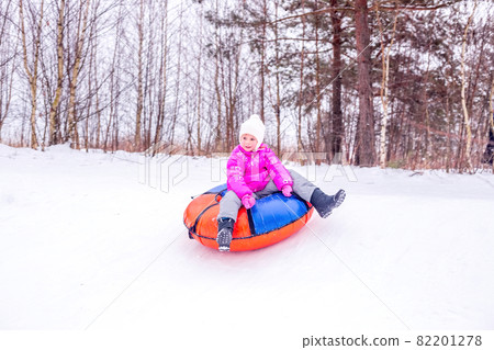A cheerful girl in warm clothes rides down snowy hill on slide-slide cheesecake 82201278