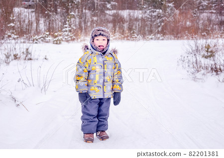 A boy in warm clothes stands in the middle of a winter forest A boy in warm clothes stands in the middle of a winter forest 82201381