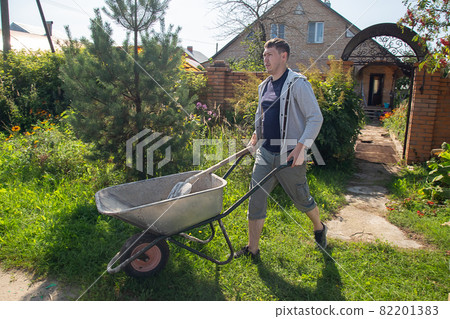 A man carries a garden wheelbarrow for loading sand to fill the paths 82201383