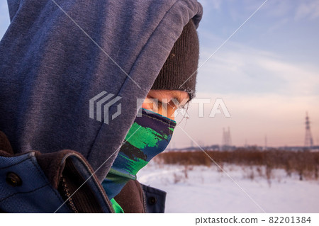 Close up view of a caucasian man face with scarf as mask and hooded jacket. Close up view of a caucasian man face with scarf as mask and hooded jacket. 82201384