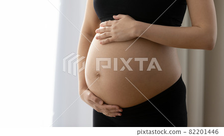 Future mom holding both hands on naked heavy pregnant belly 82201446