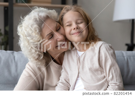 Affectionate old grandmother cuddling little grandchild at home. 82201454