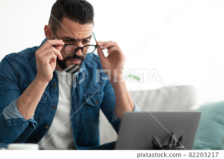 Stressed young Arab man using laptop, having difficulty performing work task, making error at home, copy space Stressed young Arab man using laptop, having difficulty performing work task, making error at home, copy space 82203217