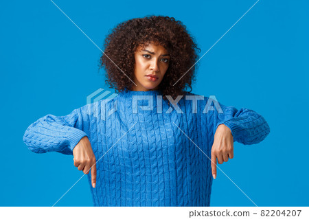 Upset and gloomy girl waiting for explanation, feeling uneasy and depressed, pointing fingers down, looking sad and unhappy camera, standing blue background distressed 82204207