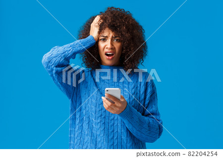 Indecisive troubled girl dont know what do, facing huge trouble. Shocked and cocnerned african-american woman in winter sweater grab head and grimace at camera, reading bad news on smartphone 82204254