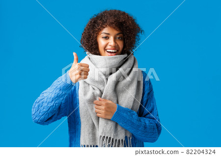 Very good, yes. Cute happy african-american woman in sweater, bought cool warm and comfortable scarf showing thumb-up in approval, recommend shop, standing blue background Very good, yes. Cute happy african-american woman in sweater, bought cool warm and comfortable scarf showing thumb-up in approval, recommend shop, standing blue background 82204324