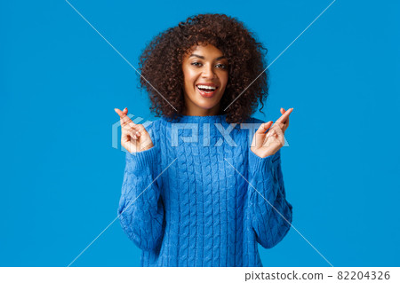 Hope my new year wishes come true. Cheerful, hopeful and optimistic beautiful african american woman in winter sweater, cross fingers for good luck and smiling excited, anticipate dream fulfill Hope my new year wishes come true. Cheerful, hopeful and optimistic beautiful african american woman in winter sweater, cross fingers for good luck and smiling excited, anticipate dream fulfill 82204326