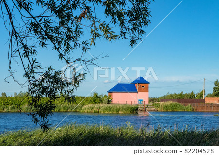 The building is a pumping station. Technical building on the shore. Little pink house on the river. The building is a pumping station. Technical building on the shore. Little pink house on the river. 82204528