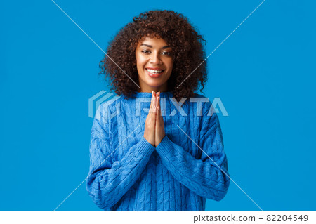 Thankful cute smiling african-american pretty woman with afro haircut, saying arigato and smiling, clasp hands together near chest looking grateful, showing respect, standing blue background Thankful cute smiling african-american pretty woman with afro haircut, saying arigato and smiling, clasp hands together near chest looking grateful, showing respect, standing blue background 82204549