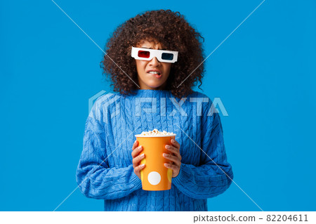 Uneasy and sad cute african-american woman with afro haircut watching favorite character dying in movie, grimacing upset and distressed, frowning wear 3d glasses in cinema, eat popcorn Uneasy and sad cute african-american woman with afro haircut watching favorite character dying in movie, grimacing upset and distressed, frowning wear 3d glasses in cinema, eat popcorn 82204611