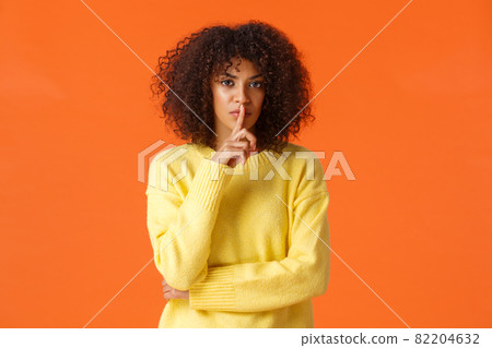 Waist-up shot mad and displeased, serious-looking african-american woman telling secret and asking swear not say a word, shushing press index finger to lips and staring angry camera, be quiet 82204632