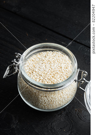 Decorticated sesame seeds, in glass jar, on black wooden background 82204947