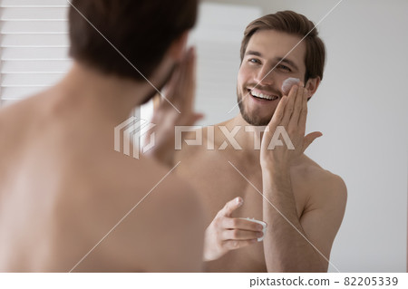 Handsome young man looks in mirror apply facial cream 82205339