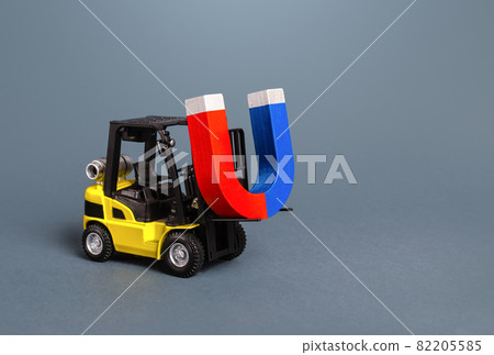 A forklift is carrying a big magnet. The concept of attraction and gravity. Attracting money and investments for startups. Increase profits and attract new customers. Salary, bonus, cashback. 82205585