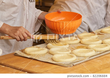The woman in the picture is making filled pies. Hands wearing protective gloves coat the pie dough with raw egg. Work in the bakery. 82206884