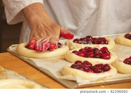 The woman in the picture is making filled fruit pies. Hands filling pie yeast dough with strawberries. Work in the bakery. 82206892