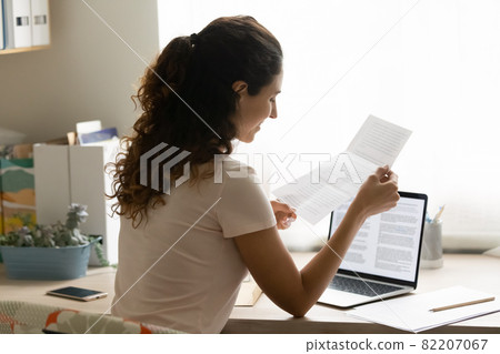 Young smiling woman sit at desk reading letter 82207067