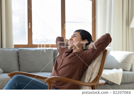 Peaceful young indian woman relax on armchair at living room 82207068