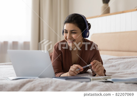 Indian female wear earphones watch training on laptop on bed Indian female wear earphones watch training on laptop on bed 82207069