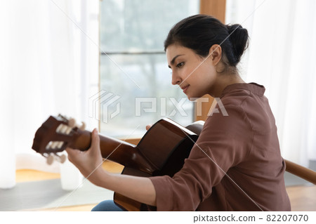 Inspired young indian female guitarist hold guitar play lyrical melody 82207070