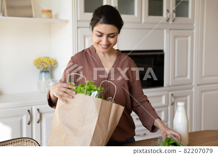 Happy indian lady put food products out of paper bag Happy indian lady put food products out of paper bag 82207079