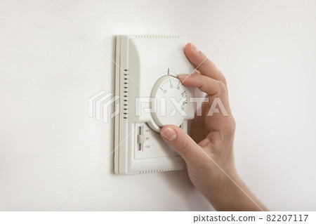 Young woman hand switch on temperature regulator on wall panel 82207117
