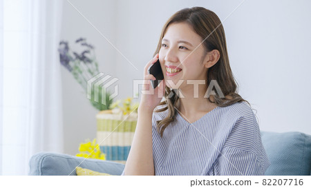 Young woman talking on her smartphone at home Young woman talking on her smartphone at home 82207716