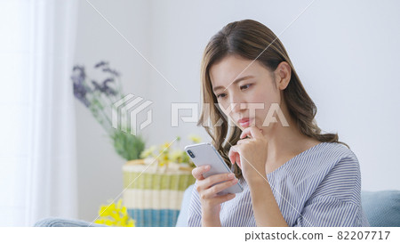 Young woman operating a smartphone at home Young woman operating a smartphone at home 82207717