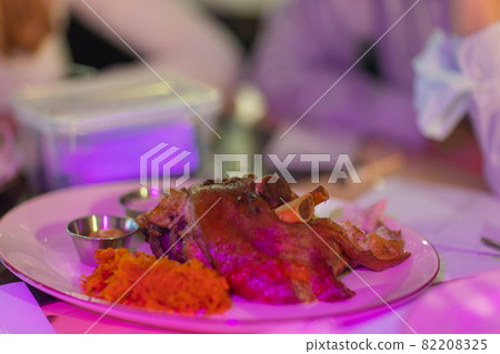 Unusual plate with pork knuckle. Unusual wooden plate with delicious pork knuckle and side dishes upon. 82208325
